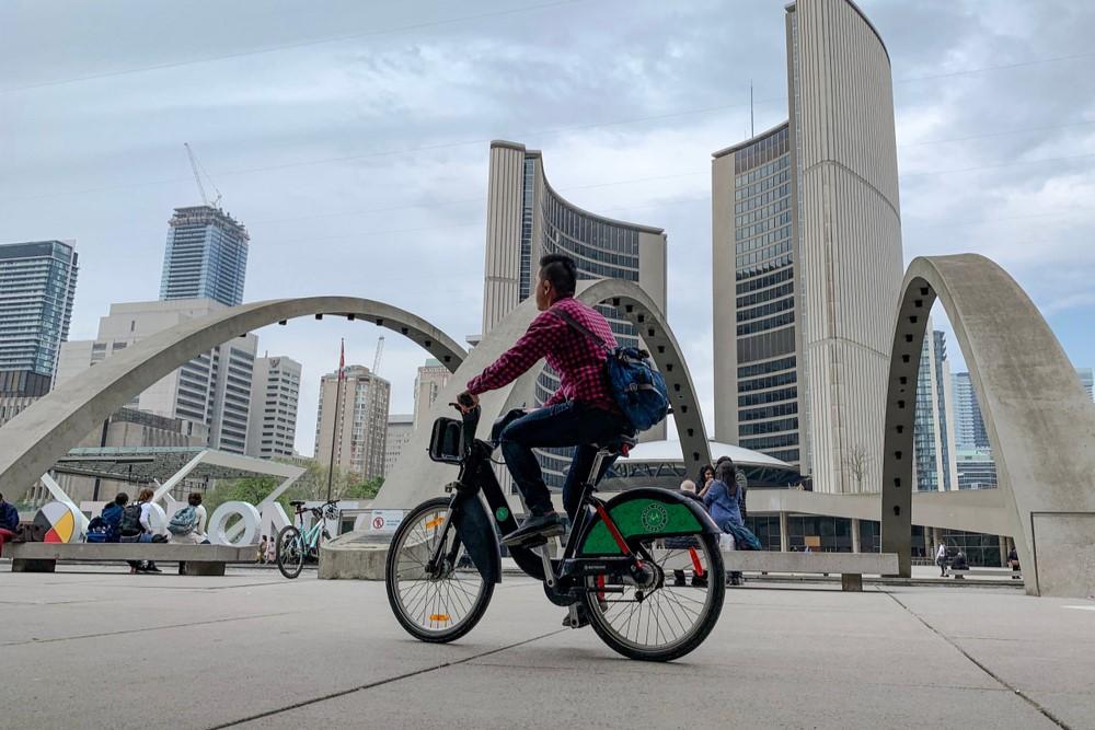 Bicycle Share Toronto. An unknown man takes advantage of a bike share program as he cycles past Toronto city hall on one of Metrolinx’s “Toronto Bike Share” bicycles.