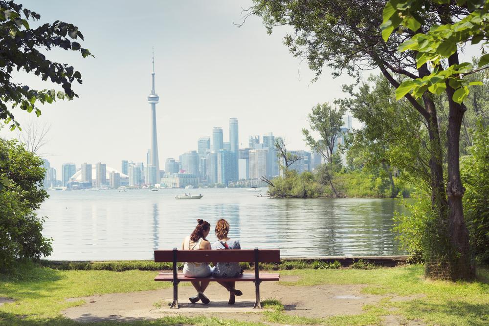 Two,Girls,Sitting,On,The,Bench,,City,View,,Background,,Toronto